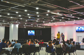 Large corporate conference hall with rows of seated attendees facing a stage with presentation screens